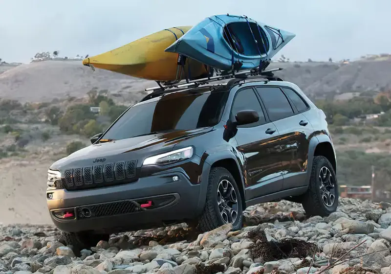 Black Jeep Cherokee off-roading on rocks with 2 kayaks on its roof